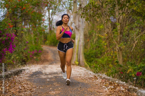 Fototapeta young happy attractive and exotic Asian Indonesian runner woman in jogging workout outdoors at countryside road track nature background running cheerful