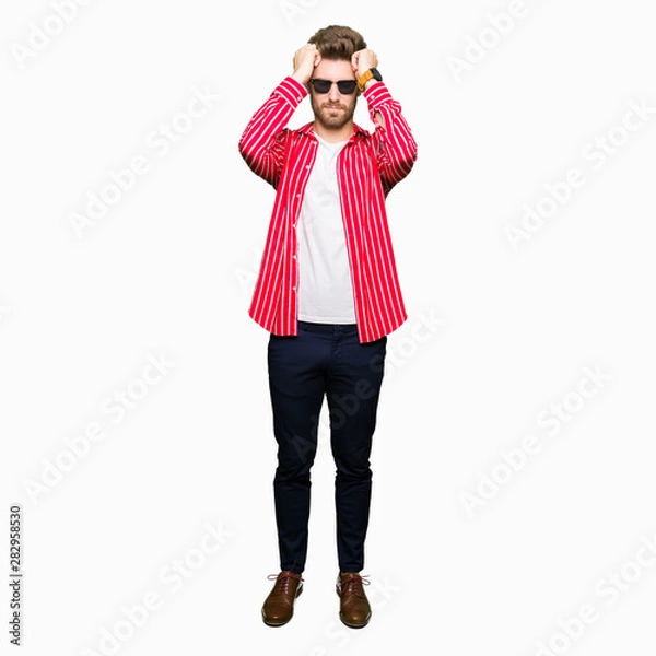 Fototapeta Young handsome man wearing sunglasses suffering from headache desperate and stressed because pain and migraine. Hands on head.