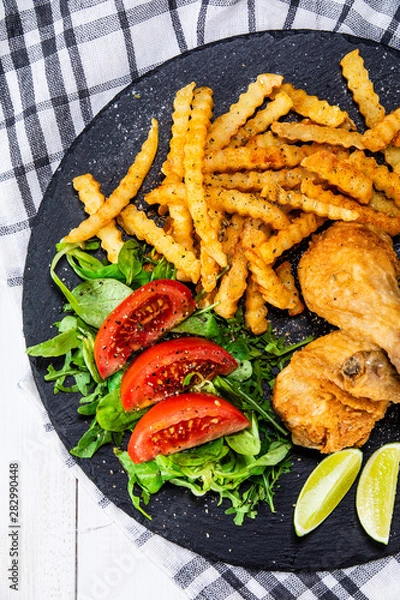 Fototapeta Grilled chicken drumsticks with french fries and vegetables