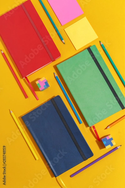 Fototapeta Composition of several stationery notebooks of different colors and stationery on a yellow background. Creative concept of stationery and school supplies. Top view