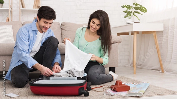 Fototapeta Loving couple packing clothes into suitcase at home