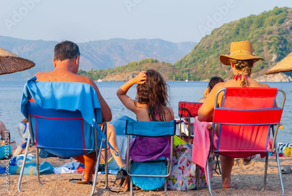 Fototapeta Three people resting on the beach. Family tourism concept