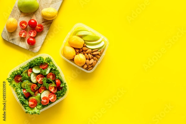 Fototapeta food container with salad and nuts, fruit on yellow background top view mockup