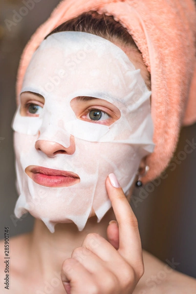 Fototapeta Face of a young woman with a tissue moisturizing cosmetic mask - cosmetic procedures