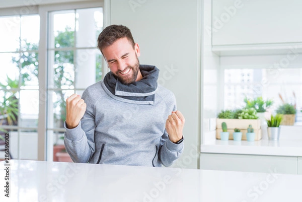 Fototapeta Handsome man at home very happy and excited doing winner gesture with arms raised, smiling and screaming for success. Celebration concept.