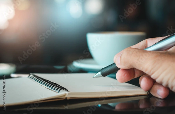 Fototapeta Closeup of hand businessman working and writing on notebook with smartphone and drink coffee in cafe