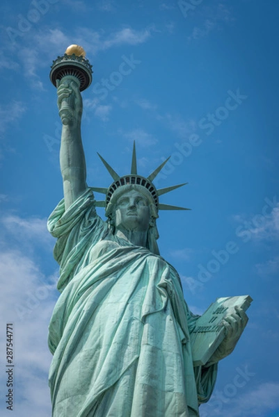 Fototapeta Shot of the Statue of Liberty in New York City, Usa. The shot is taken during a beautiful sunny day with a blue sky and white clouds in the background	