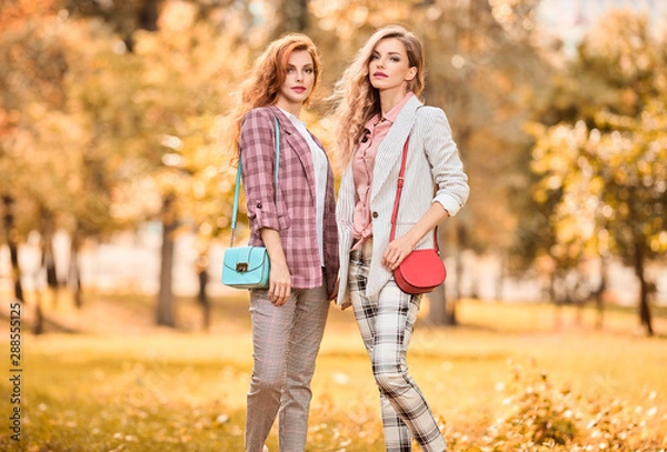 Fototapeta Autumn fashion outdoor. Two Young Beautiful happy woman walking at fall park, enjoy nature. Joyful Model girl friends smiling have a good time, fashionable stylish jackets, pants, autumnal lifestyle