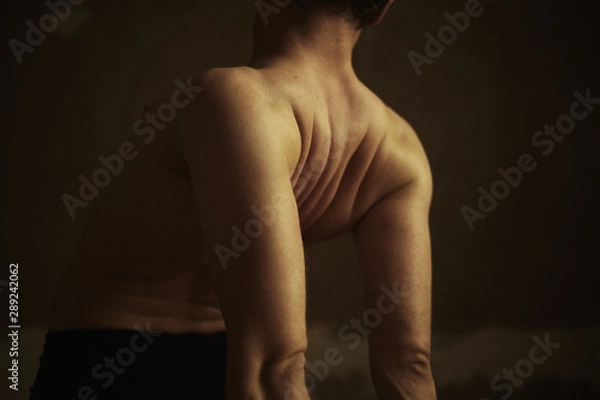 Fototapeta Authentic horizontal closeup shot of fit man. Strong male practicing yoga in dark intimate atmosphere, standing calm in asana. Film grain effect. Handsome athletic body in motion captured indoors