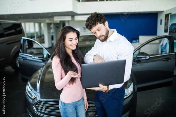 Fototapeta Sales manager showing something on a laptop to the smiling customer near car