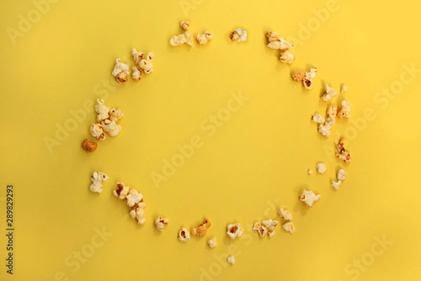 Fototapeta flavored popcorn scattered on an oval yellow background, copy space in the center