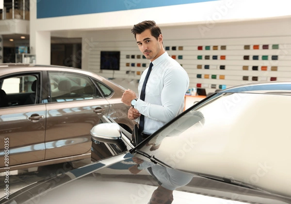 Fototapeta Young salesman near new car in modern dealership