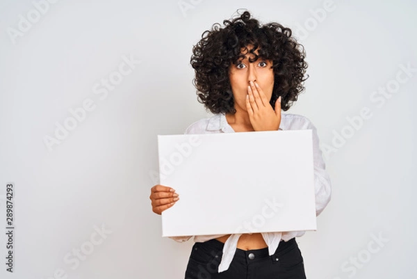 Fototapeta Young arab woman with curly hair holding banner over isolated white background cover mouth with hand shocked with shame for mistake, expression of fear, scared in silence, secret concept