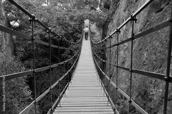 Fototapeta Hombre mayor caminando sobre un puente colgante de hierro y tablas de madera