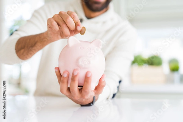 Fototapeta Man putting a coin inside of piggy bank saving for investment