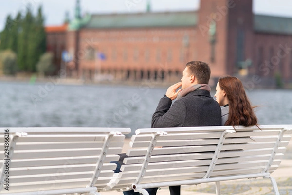 Fototapeta Young couple sitting on a waterfront bench