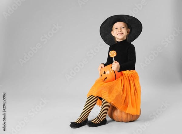 Fototapeta Cute little girl with pumpkin candy bucket and lollipop wearing Halloween costume on grey background. Space for text