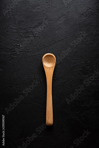 Fototapeta Empty new clean small bamboo wooden spoon on black dark table background top view flat lay.