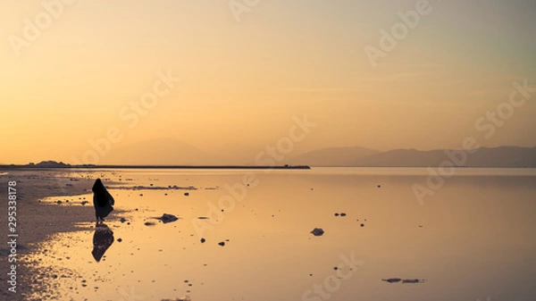 Fototapeta Silhouette and reflection of an unidentified Iranian woman in hijab burka near Maharloo pink lake, Shiraz, Iran