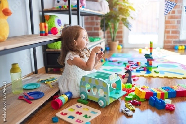 Fototapeta Adorable blonde toddler playing around lots of toys at kindergarten