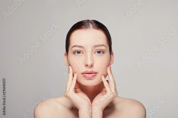 Fototapeta girl with brown hair clean fresh skin naked shoulders holding hand on face posing at gray studio background, a model with light nude make-up, copy space.