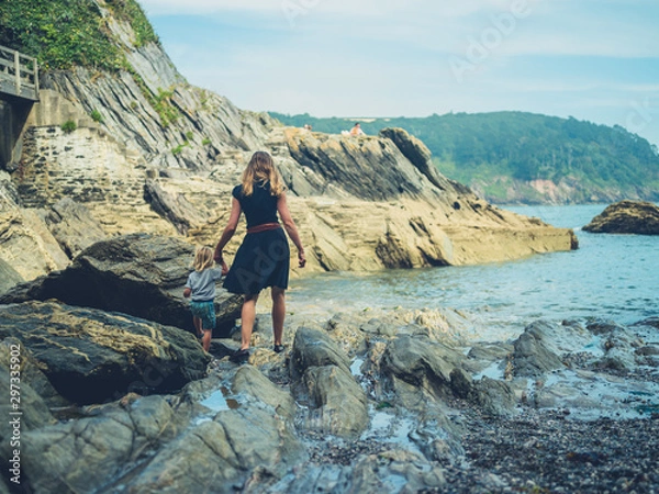 Fototapeta Young mother and toddler walking on rocks by the beach