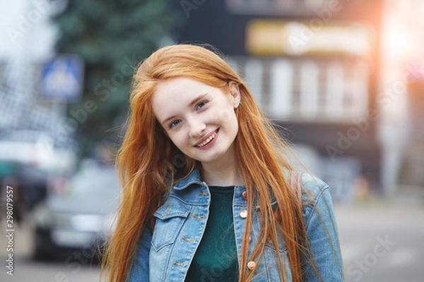 Fototapeta candid outdoor portrait of pretty smiling young girl with long red hair, morning sunrise light