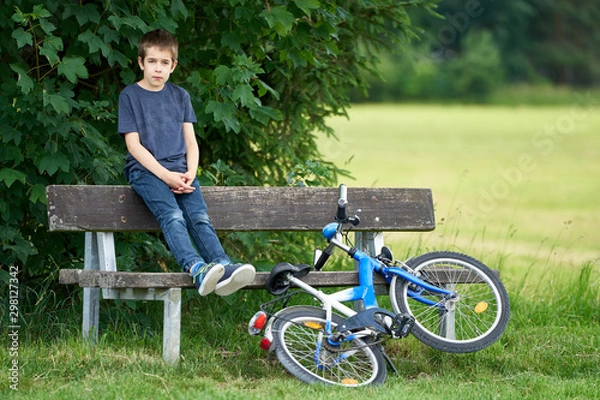 Fototapeta A boy relaxs on a bench in a field and a bicycle nearby