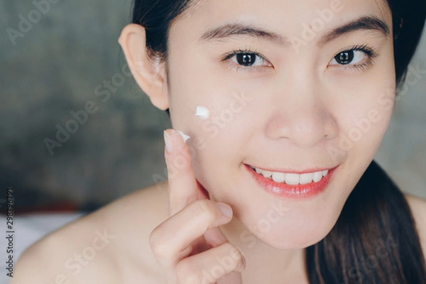 Fototapeta Cropped shot view of young Asian woman applying acne cream/moisturizer on her face. Conceptual of beauty and cosmetic.