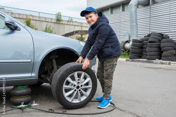 Fototapeta Children's auto mechanic changes the wheel on a car. Replacing wheels on a car.