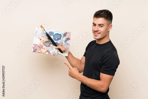 Fototapeta Young artist man over isolated background and pointing it