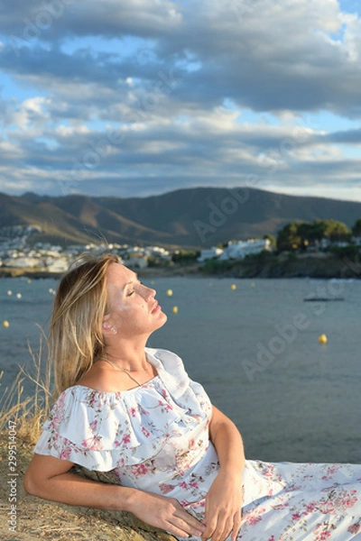 Fototapeta Woman sitting in front of a coastal landscape of the northern mediterranean on a summer afternoon with wind taking a sunbath with copy space