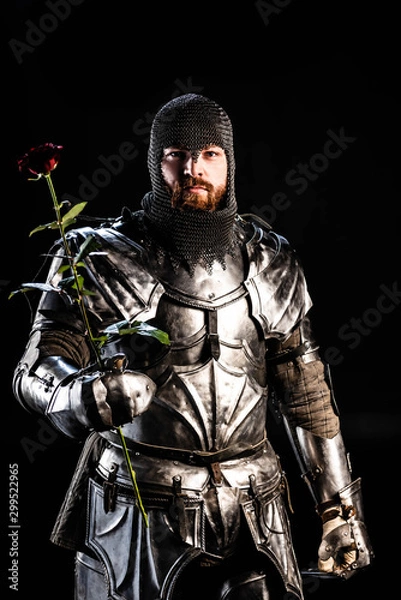 Fototapeta handsome knight in armor holding rose isolated on black