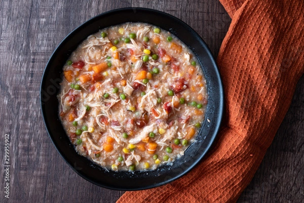 Fototapeta Puerto Rican Chicken Rice Soup in a black stoneware bowl on a dark wood table, with orange cloth napkin