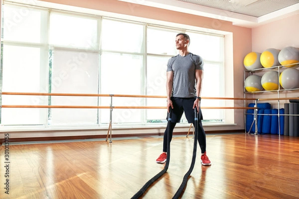 Fototapeta Young man working out with battle ropes at a gym