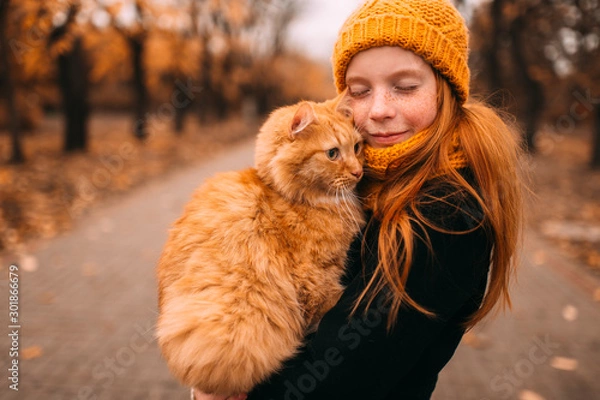 Fototapeta Beautiful freckles girl holding her loving kitten in a valley of autumn park.