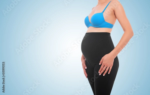 Fototapeta The body of a pregnant young woman on a blue background.