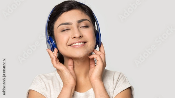 Fototapeta Smiling satisfied Indian girl in headphones enjoying favorite music