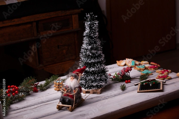 Fototapeta Santa Claus on a sleigh photographed on a white wooden background next to Christmas tree