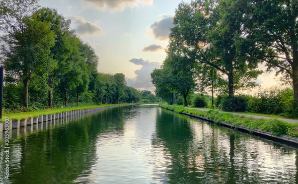 Fototapeta Beautiful and dramatic sunset or sunrise with colorful clouds and light rays in the sky over the river or canal with reflections on the water 