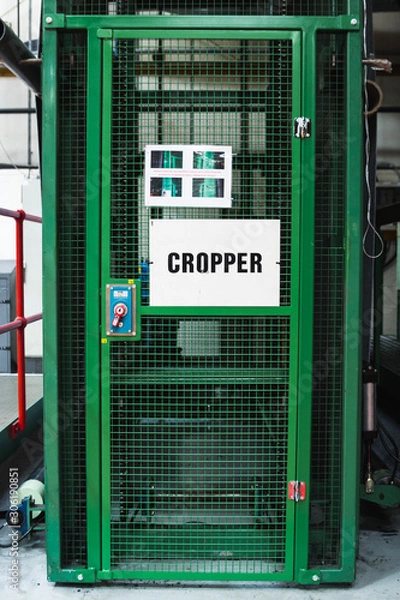 Fototapeta Bright, deep green coloured door in a factory industrial industry environment with big red emergency health and safety button for safe access and exit mesh door heavy metal security