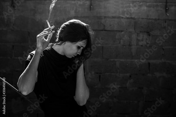 Obraz Beautiful girl smokes a cigarette in a dark building. Black and white photo