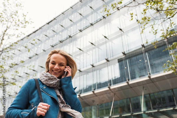 Fototapeta Executive working with a mobile phone in the street with office buildings in the background