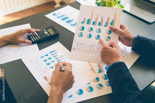 Fototapeta Businessman analysis on Graph data paper  using calculator, finance concept in office.