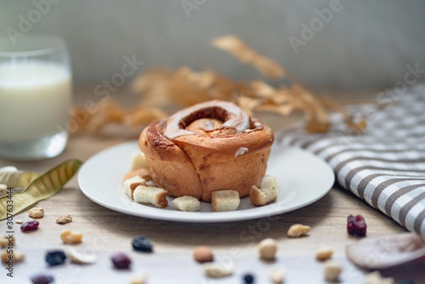 Fototapeta Plate with tasty cinnamon bun and a glass of milk on wooden table