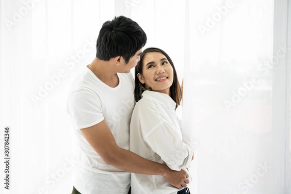 Fototapeta Asian young couple's portrait, a couple standing and talking near the window in the morning.