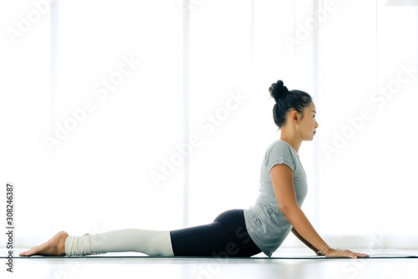 Obraz Asian yogi woman practicing yoga concept, stretching in Cobra exercise, Bhujangasana pose, working out, indoor full length, white yoga studio ,concept of healthy life and natural balance