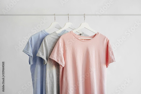 Fototapeta T-Shirts in pastel color on hanger on white background. Basic female clothes. Spring/summer outfit.