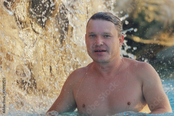 Fototapeta A man bathes in the spray of a waterfall