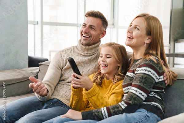 Fototapeta Image of caucasian happy family watching television on sofa at home